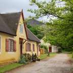Ein gelbes Haus mit einem strohdach und roten Fensterläden