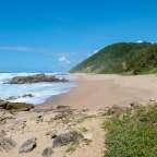 Ein sandiger Strand mit einem felsigen Hügel im Hintergrund