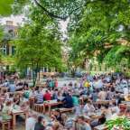 Eine Gruppe von Menschen sitzt an Holztischen in einem Park