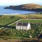 Luftaufnahme einer Kirche mit Friedhof und Strand im Hintergrund