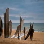 Eine Reihe von Metallskulpturen auf einem Sandstrand mit dem Ozean im Hintergrund