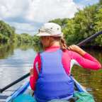 Eine Frau paddelt mit einem blauen Paddel auf einem Fluss