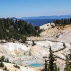 Eine Holzbrücke führt durch einen Bergtal mit Blick auf die Berge