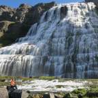 Ein Mann sitzt auf einem Felsen vor einem Wasserfall