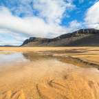 Ein Fluss fließt durch einen Sandstrand mit einem Berg im Hintergrund