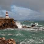 Ein rot-weißer Leuchtturm steht auf einer Klippe über dem Ozean