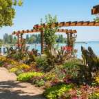 Eine hölzerne Pergola umgibt einen Blumengarten mit Blick auf einen See