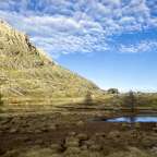 Ein Bergsee mit einem Berg im Hintergrund und einem blauen Himmel mit Wolken