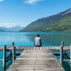 Eine Frau sitzt auf einem Dock und schaut auf einen See mit Bergen im Hintergrund