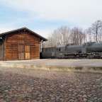 Eine schwarze Lokomotive steht vor einem Holzgebäude