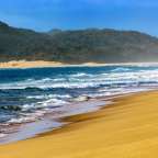 Wellen brechen an einem Strand mit Bergen im Hintergrund