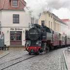 Ein Zug mit der Nummer 99 2321 0 fährt durch eine Stadtstraße