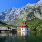 Eine kleine weiße Kirche mit rotem Dach sitzt auf einem See