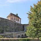 Ein kleines Gebäude mit einem Turm darauf steht neben einer Steinmauer