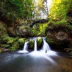 Ein Wasserfall im Wald mit einer Holzbrücke darüber