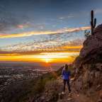 Eine Frau steht auf einem Berg mit Blick auf eine Stadt bei Sonnenuntergang