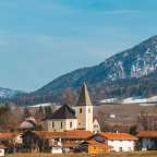 Ein Dorf mit einer Kirche im Vordergrund und einem schneebedeckten Berg im Hintergrund