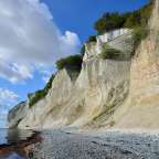 Eine Klippe mit Bäumen darauf steht über einem Kiesstrand