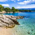 Ein felsiger Strand mit klarem Wasser und Bergen im Hintergrund