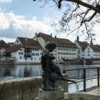 Eine Statue einer Frau sitzt neben einem Fluss