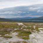 Ein Pfad führt durch eine felsige Landschaft mit Bergen im Hintergrund