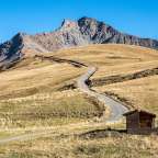 Ein Schotterweg führt durch eine trockene Wiese mit einem Berg im Hintergrund
