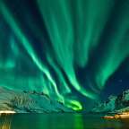 Das Nordlicht scheint über einem See mit schneebedeckten Bergen im Hintergrund