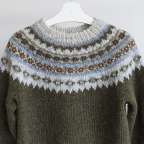 Ein grüner Pullover hängt an einem weißen Kleiderbügel