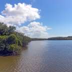 Ein Fluss mit Bäumen an der Seite und einem blauen Himmel mit Wolken