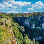 Eine Hängebrücke führt über eine Klippe mit einem Wasserfall im Hintergrund