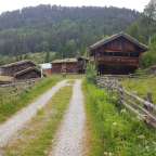 Ein Schotterweg führt zu einem Holzhaus mit Grasdach