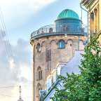 Ein Turm mit einer grünen Kuppel steht zwischen zwei Gebäuden