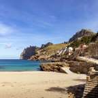 Die Bucht Cala Sant Vicenç auf Mallorca zeigt einen Sandstrand und Häuser am Fuße schroffer Berge.