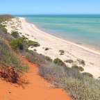 Ein Strand mit rotem Sand und grünem Wasser