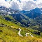 Eine kurvenreiche Straße führt durch eine grüne Bergkette