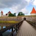 Eine Holzbrücke führt zu einem Schloss mit einem roten Turm