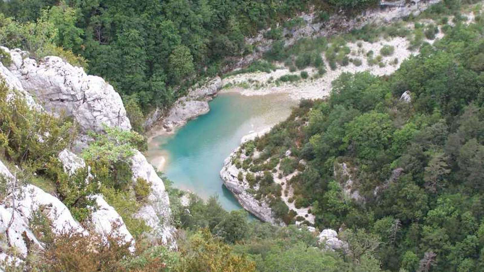 Der Blick von oben auf eine türkisfarbene Schlucht mit bewaldeten Hängen und Felsen.