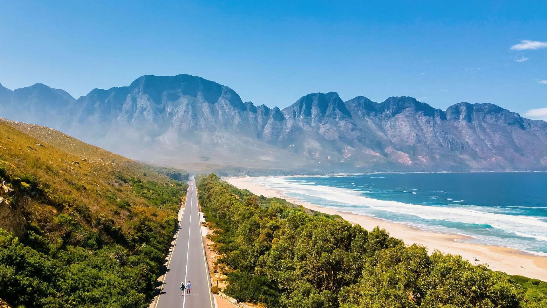 Ein Paar geht auf einer Straße in Richtung der Berge und des Ozeans.