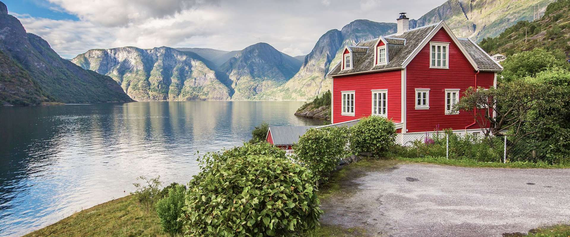 Ein rotes Haus steht an einem See mit Bergen im Hintergrund