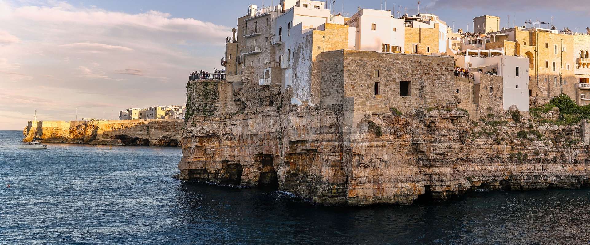 Ein Dorf mit weißen Häusern ist auf einer Klippe am Meer gebaut, das im Abendlicht beleuchtet wird.