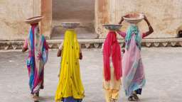 Vier Frauen in bunten Saris tragen Schüsseln auf ihren Köpfen