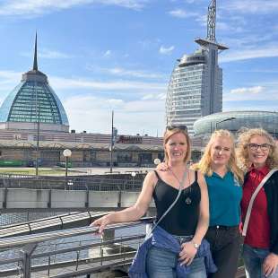 Drei Frauen stehen auf einer Brücke mit einem großen Gebäude im Hintergrund