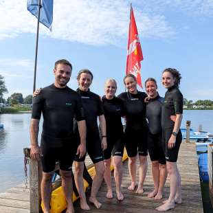 Eine Gruppe von Menschen steht auf einem Dock und trägt wetsuits