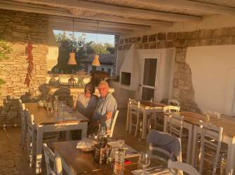 Zwei Personen sitzen an einem Tisch in einem Restaurant im Freien, das bei Sonnenuntergang beleuchtet wird.