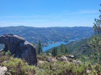 Ein Panorama von bergigen Landschaften mit einem blauen Fluss, der sich durch das Tal schlängelt, und felsigen Vorsprüngen im Vordergrund.