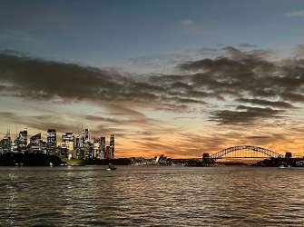 Eine beleuchtete Skyline von Sydney im Abenddämmerungshimmel mit dem Sydney Harbour Bridge.