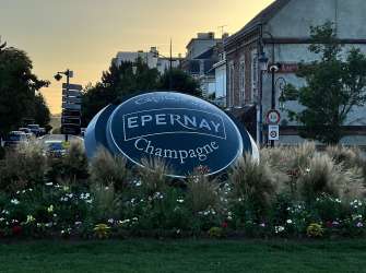 Ein Schild mit der Aufschrift "EPERNAY Champagne" und Blumenbeete vor Gebäuden und Bäumen.