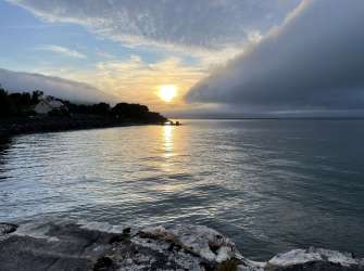 Ein Sonnenuntergang über dem Wasser mit einer bewohnten Küste und einer großen Wolkenformation.