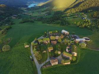 Ein malerisches Dorf mit traditionellen Gebäuden, die mit grünen Grasdächern gedeckt sind, liegt eingebettet in einer weitläufigen grünen Landschaft.