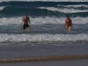 Zwei Personen stehen im Meer und es brechen Wellen.